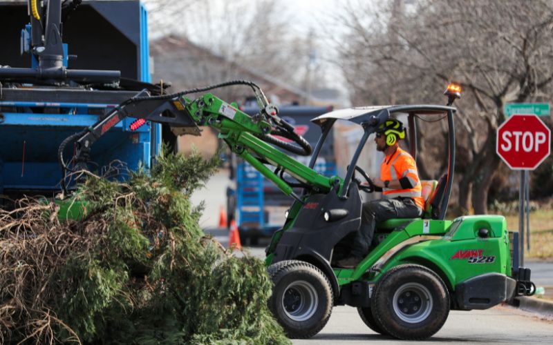 A member of the Godspeed Tree Service ground crew moves debris from a tree removal to the chipper.