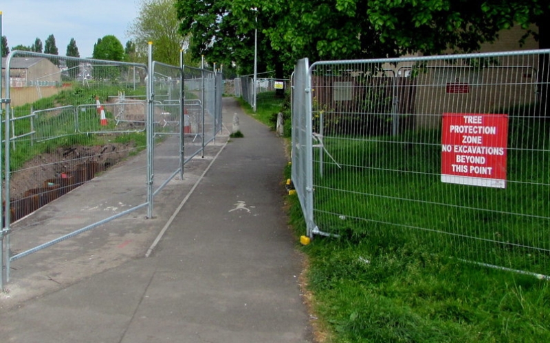 Metal fencing separating mature trees from the paved path and a trench being dug in a Winston-Salem neighborhood. A red sign warns “Tree Protection Zone – No Excavations Beyond This Point.”