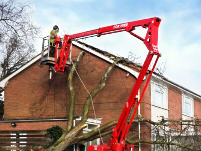 An arborist in a bucket truck, removing a tree growing alongside a home in North Carolina.