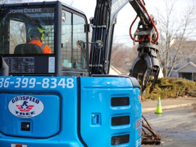 Godspeed Tree Service operator in a blue John Deere skid steer uses a grapple attachment to remove storm debris in a Winston-Salem neighborhood.