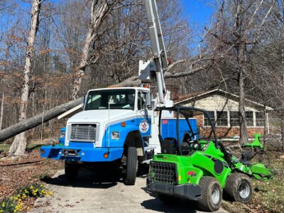 Godspeed's professional tree service bucket truck and green stump grinder positioned at a residential property during emergency tree removal cleanup in Winston-Salem.