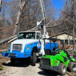 Godspeed's professional tree service bucket truck and green stump grinder positioned at a residential property during emergency tree removal cleanup in Winston-Salem.